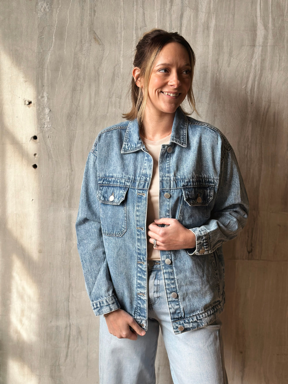 Person wearing a denim jacket standing against a wooden wall