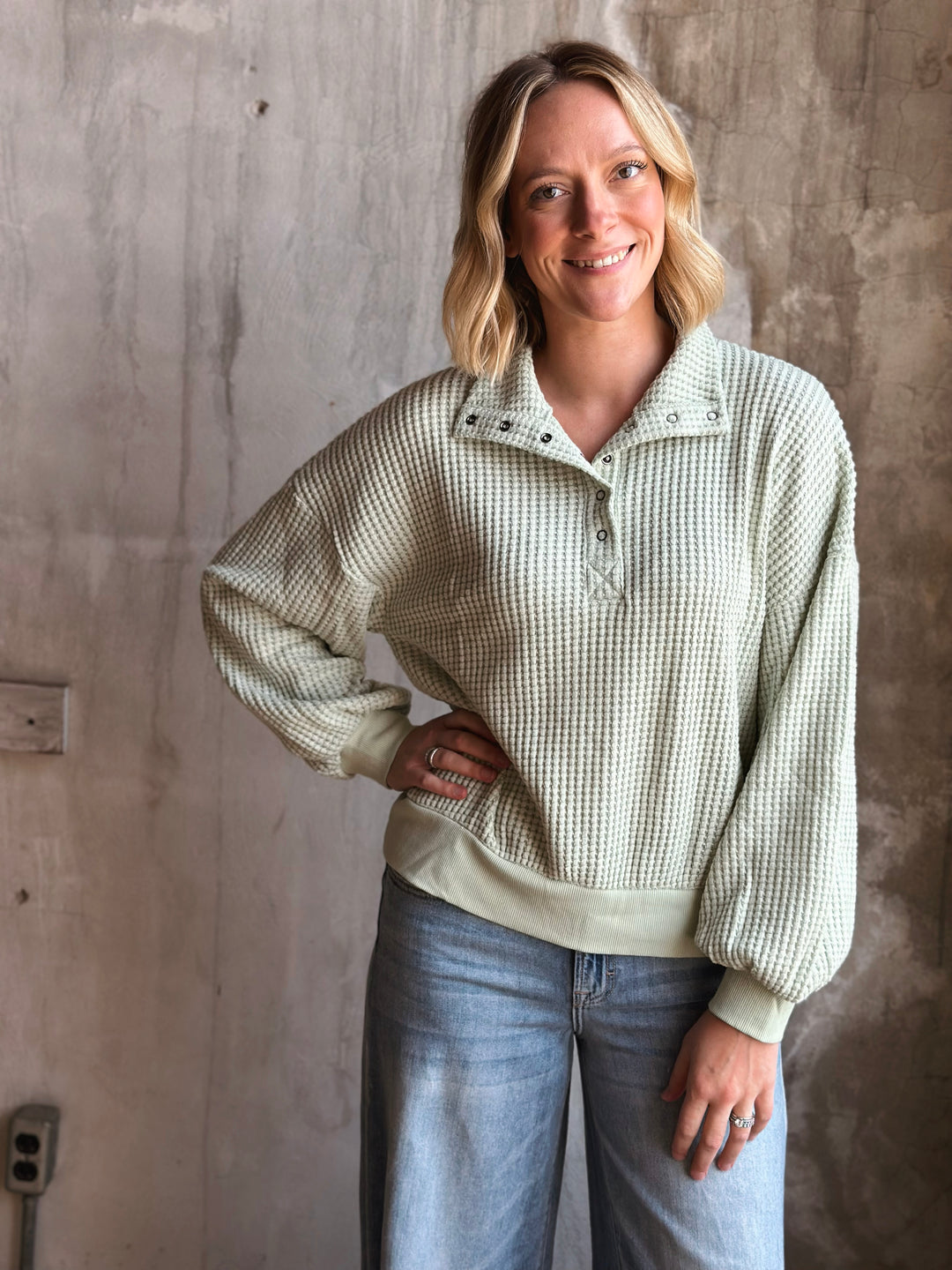 Woman wearing a light green checkered sweater against a textured wall.