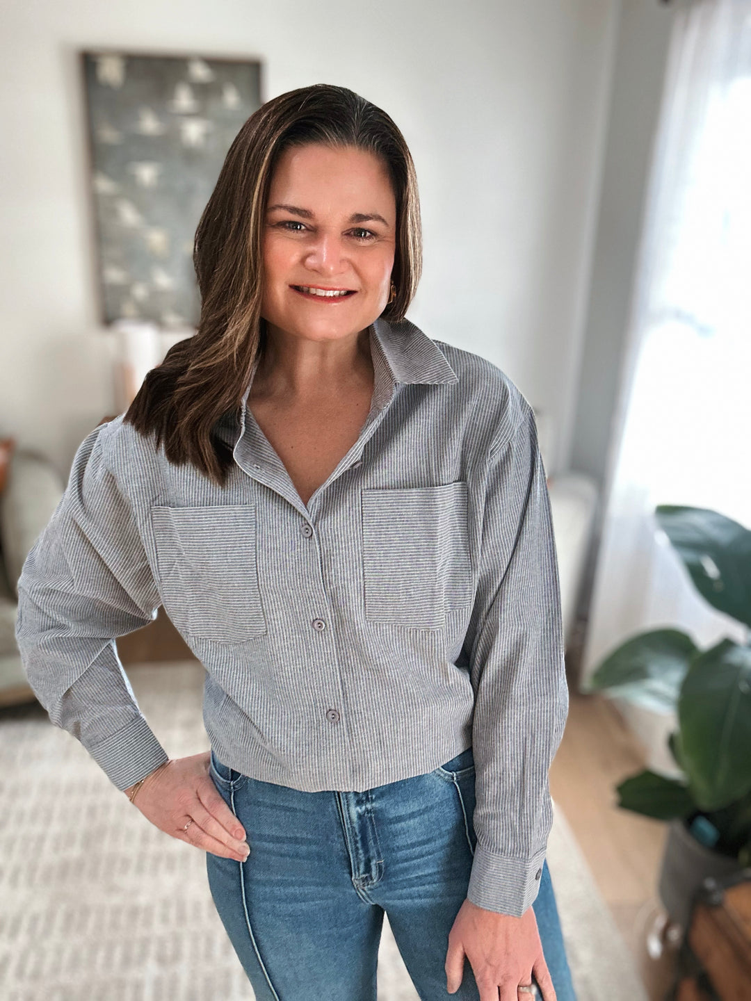 Woman wearing a gray striped shirt and blue jeans indoors.