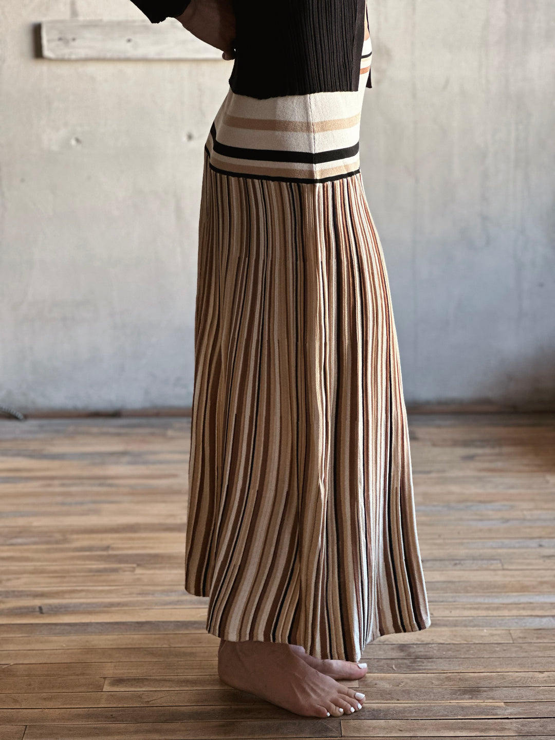 Person wearing a pleated skirt with a striped pattern on a wooden floor.