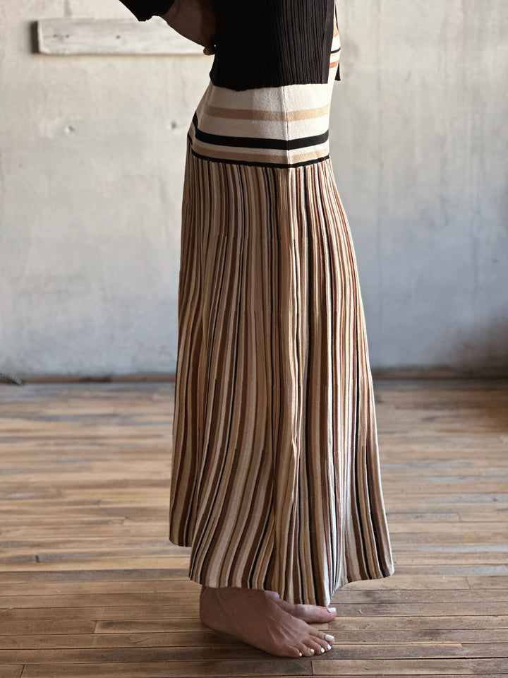 Person wearing a pleated skirt with a striped pattern on a wooden floor.