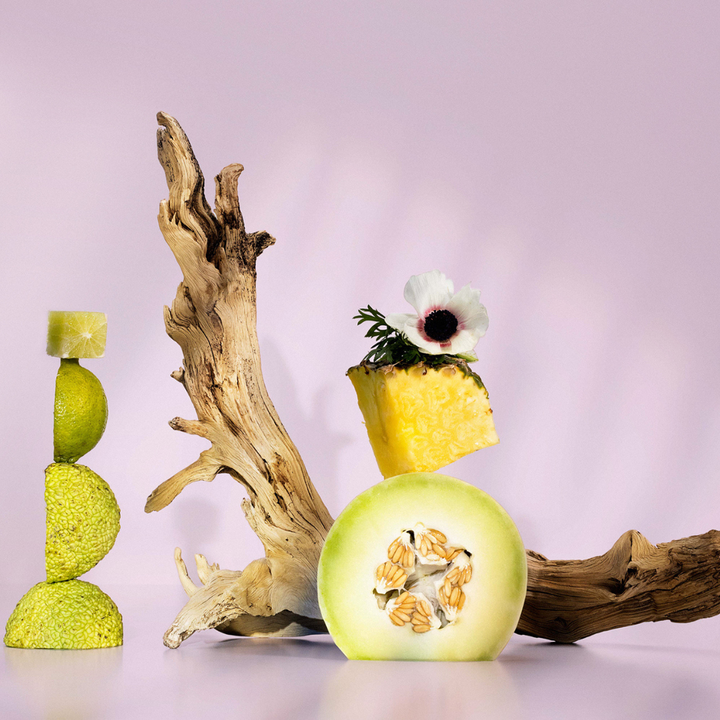 Decorative arrangement with a honeydew melon, pineapple, and green candle on a purple background