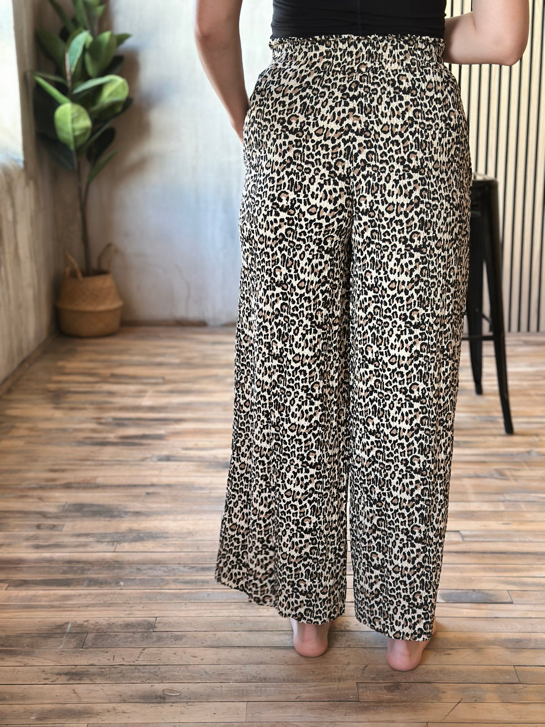 Person wearing leopard print pants standing on a wooden floor with a plant in the background