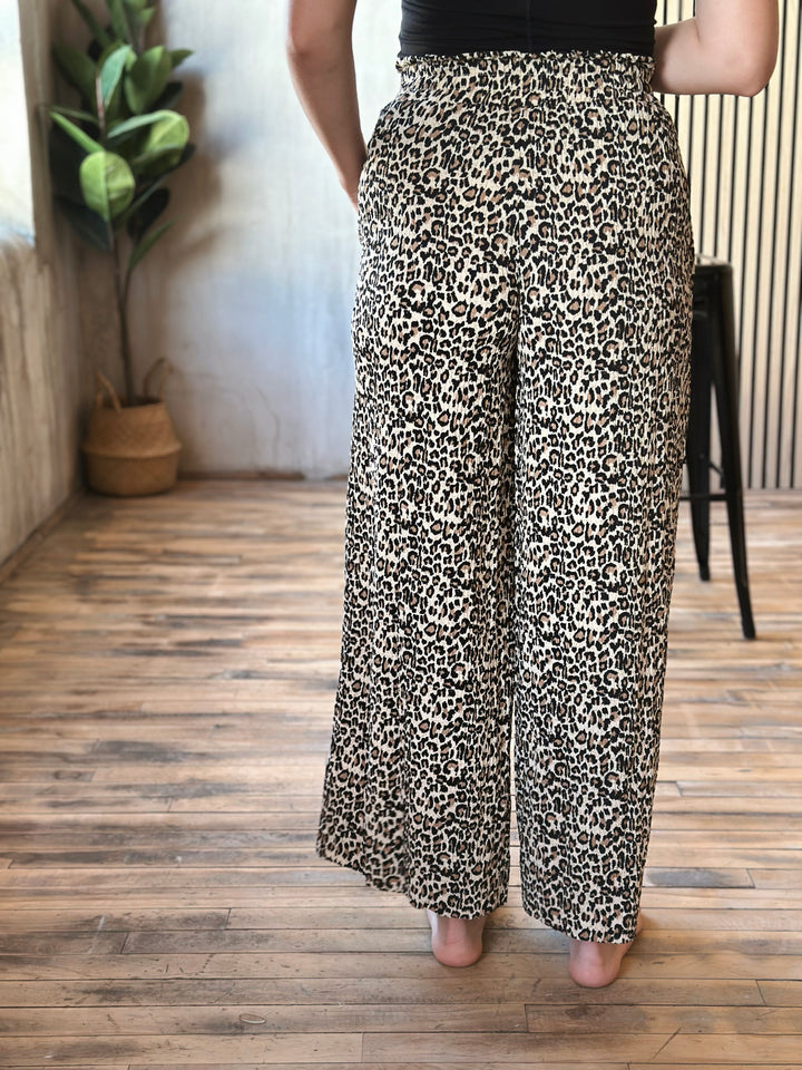 Person wearing leopard print pants standing on a wooden floor with a plant in the background