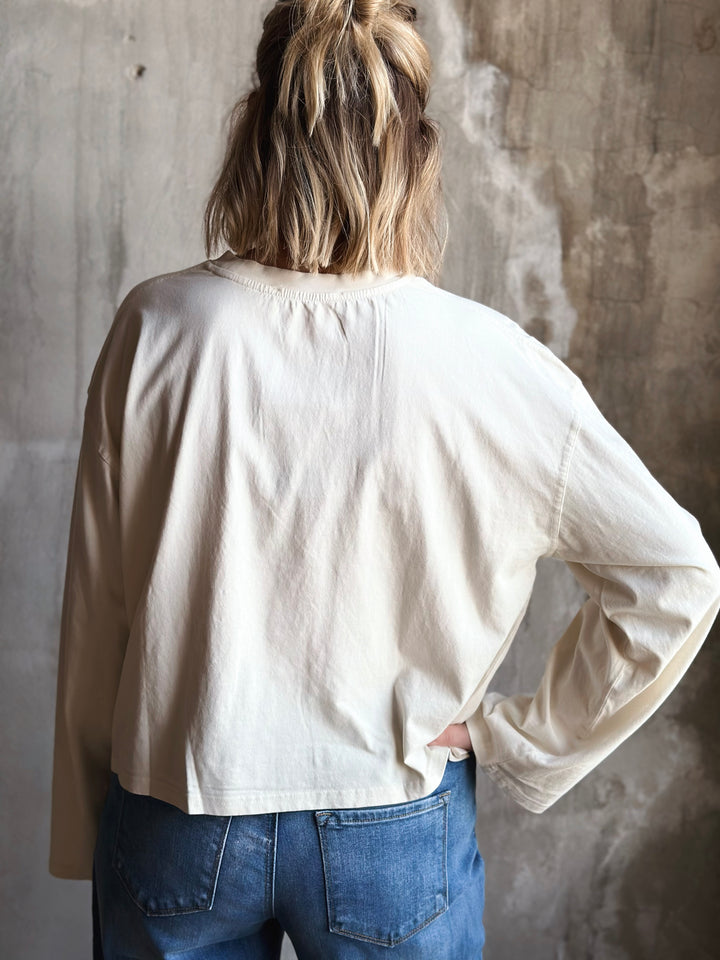 Person wearing a beige shirt and blue jeans against a textured wall.