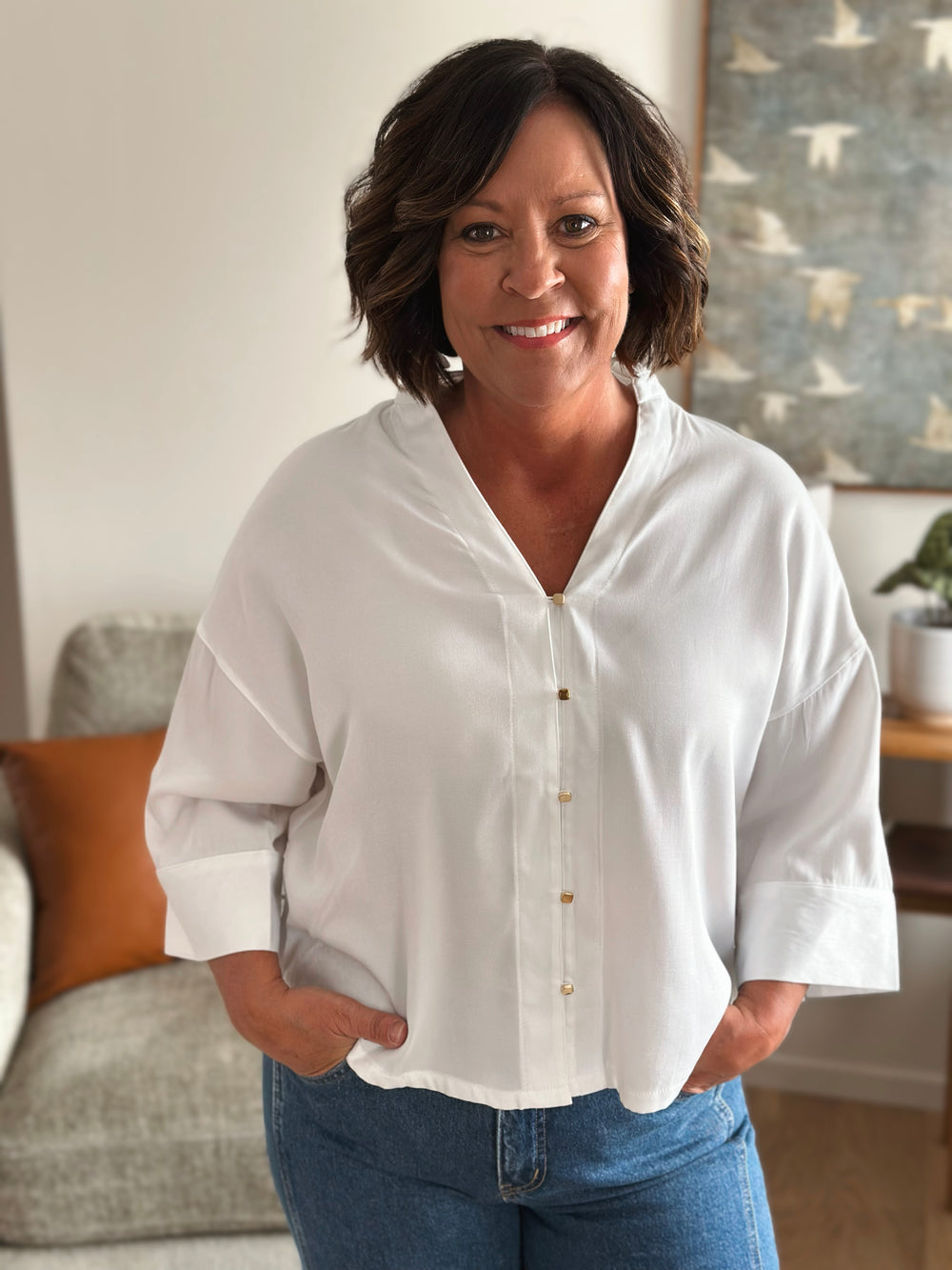 Woman wearing a white blouse and blue jeans standing in a living room.