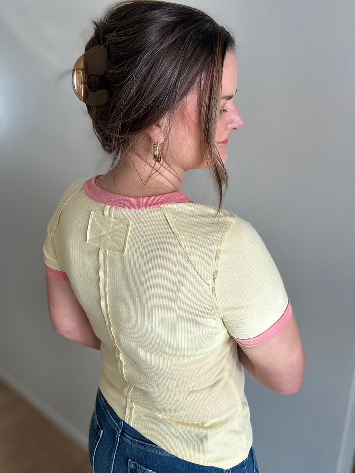 Woman wearing a light yellow shirt with pink trim against a plain background