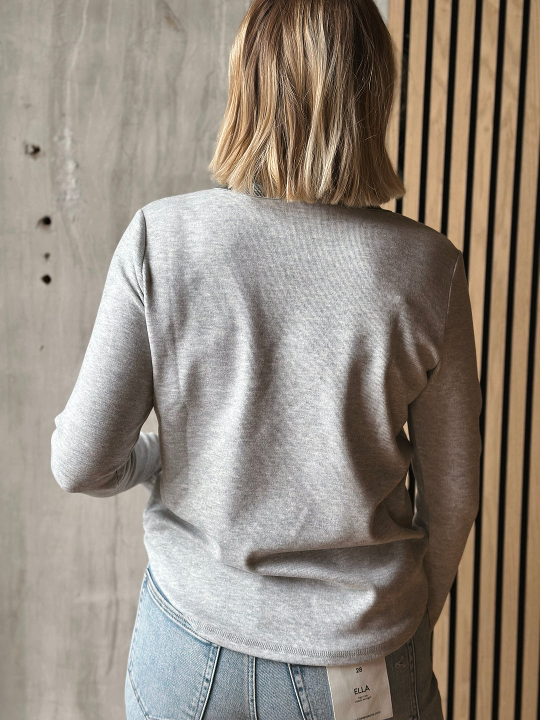 Person wearing a gray sweater and jeans against a wooden wall.