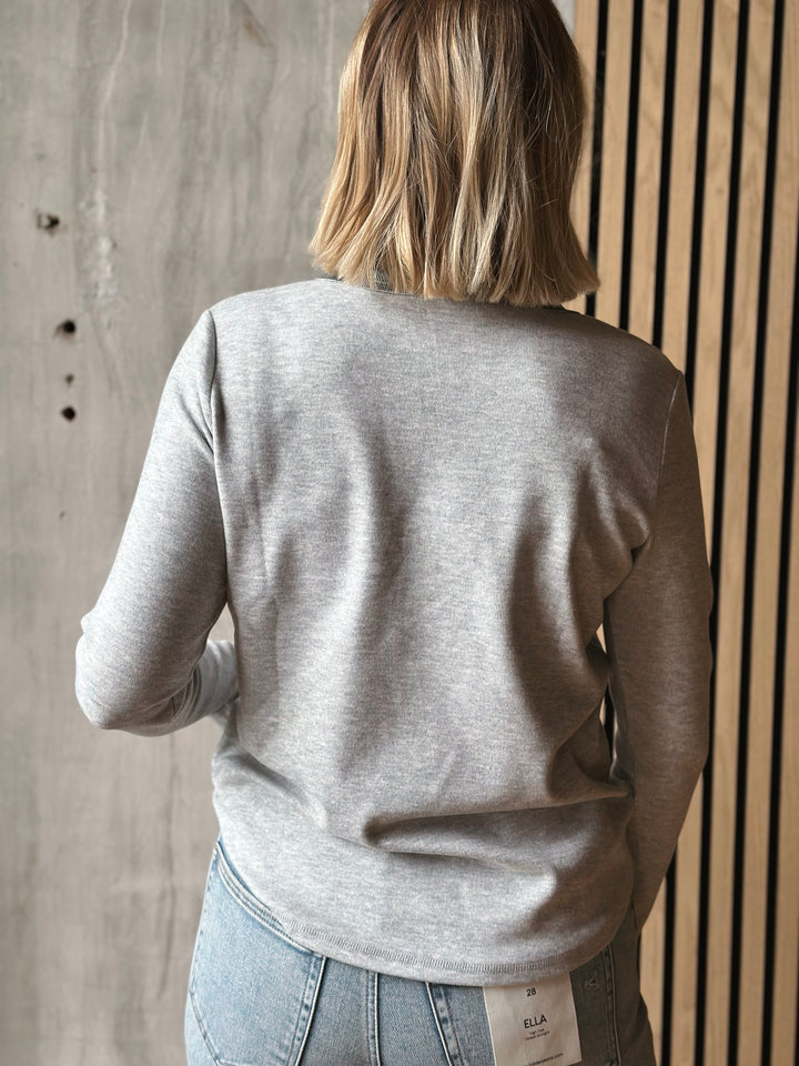 Person wearing a gray sweater and jeans against a wooden wall.