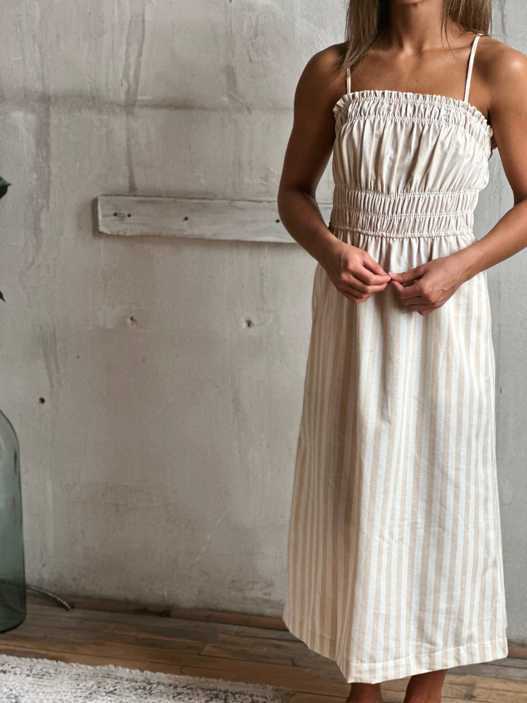 Woman wearing a white and cream striped dress against a gray wall.