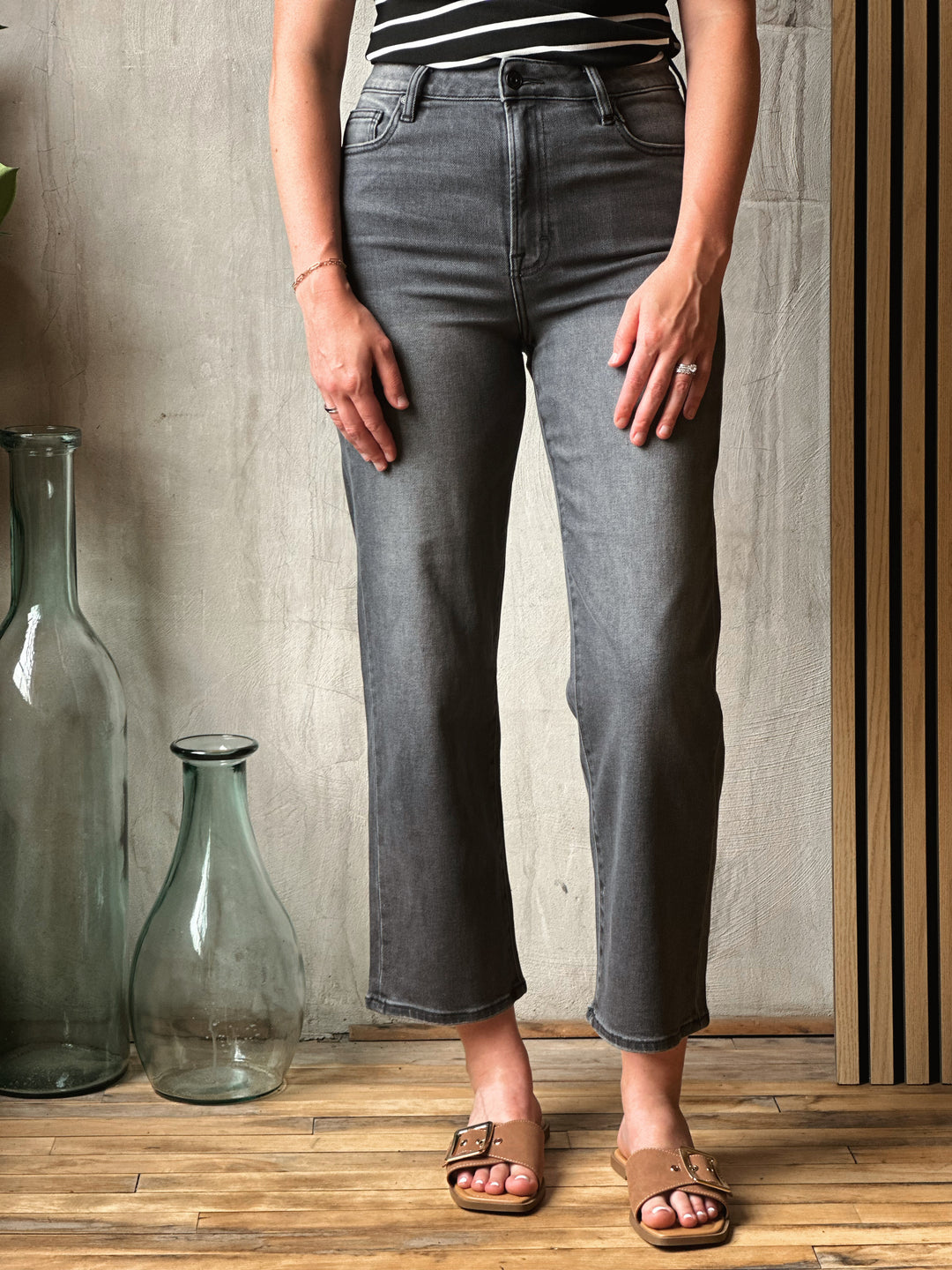 Person wearing gray jeans standing in a room with wooden floor and textured wall.