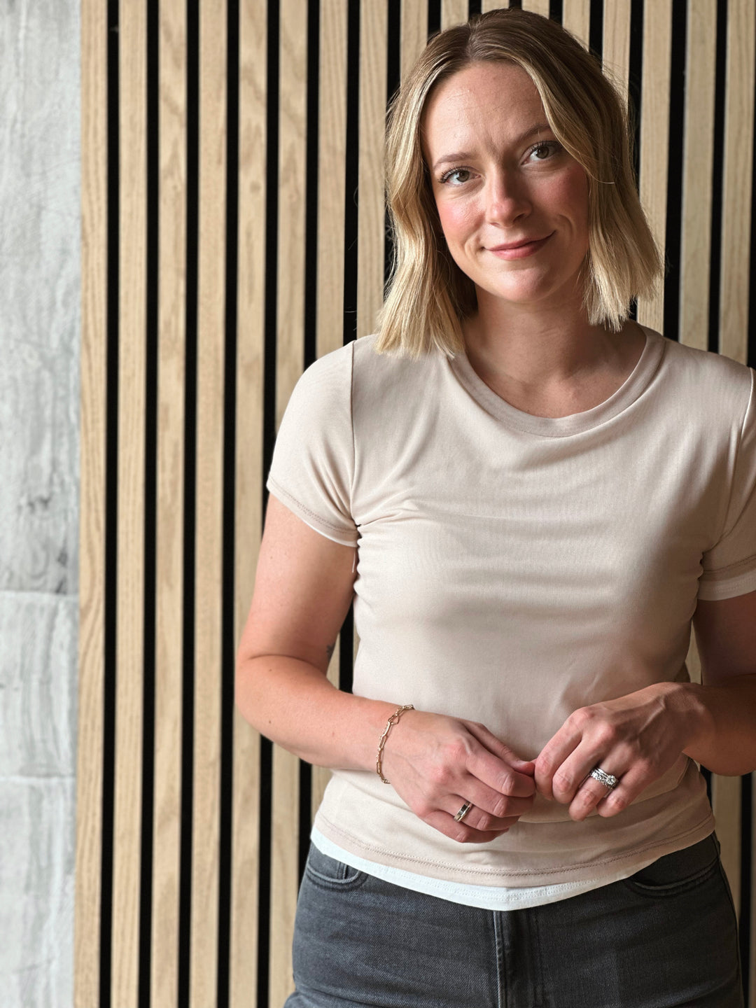 Woman wearing a white t-shirt and jeans standing against a striped wall.
