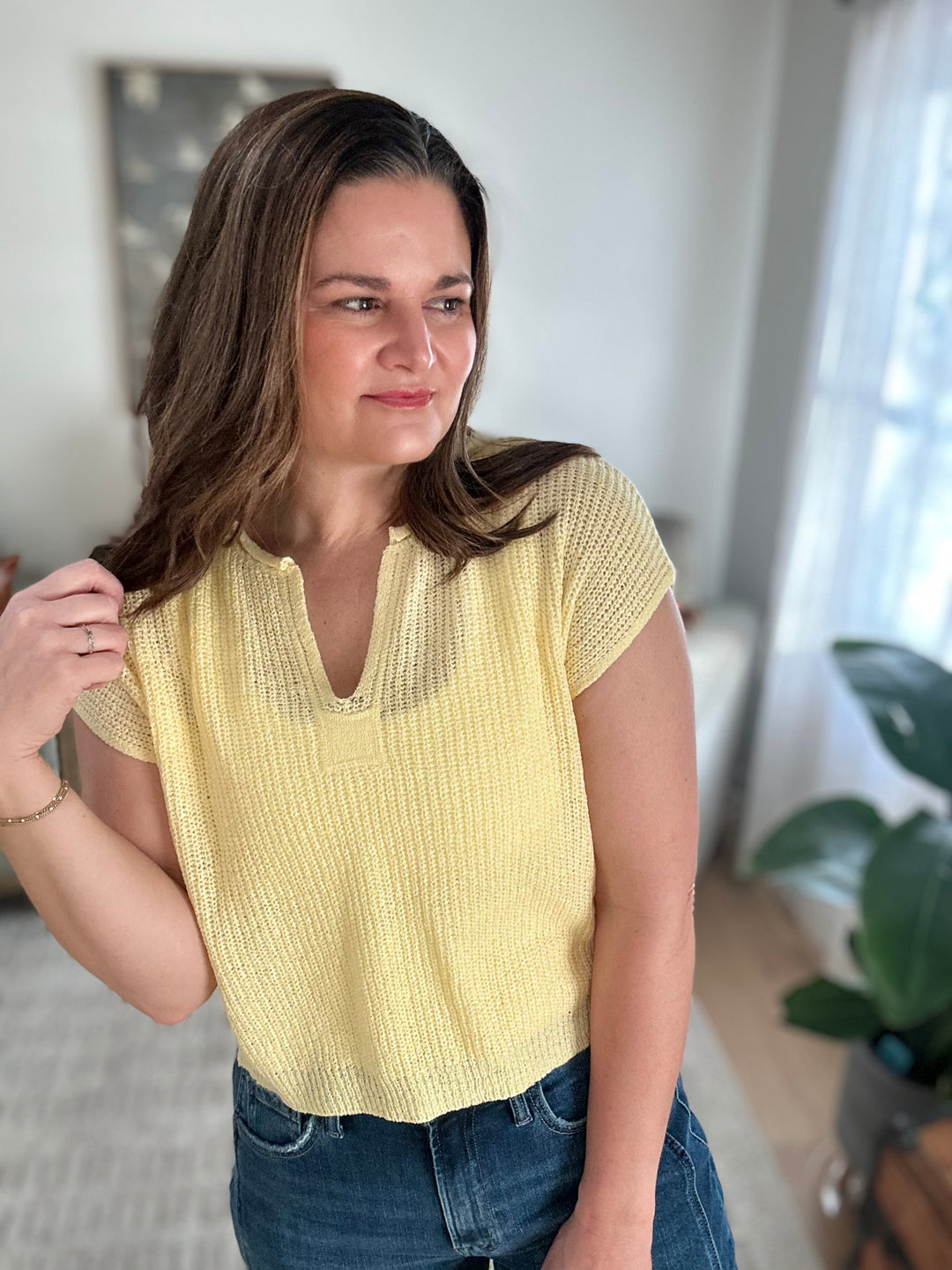 Woman wearing a yellow knitted top and blue jeans indoors.