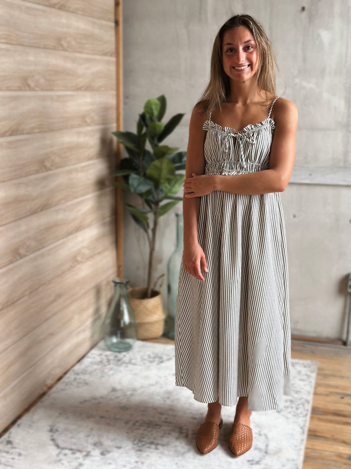 Woman wearing a white and gray striped dress standing in a room with a wooden floor and plant.