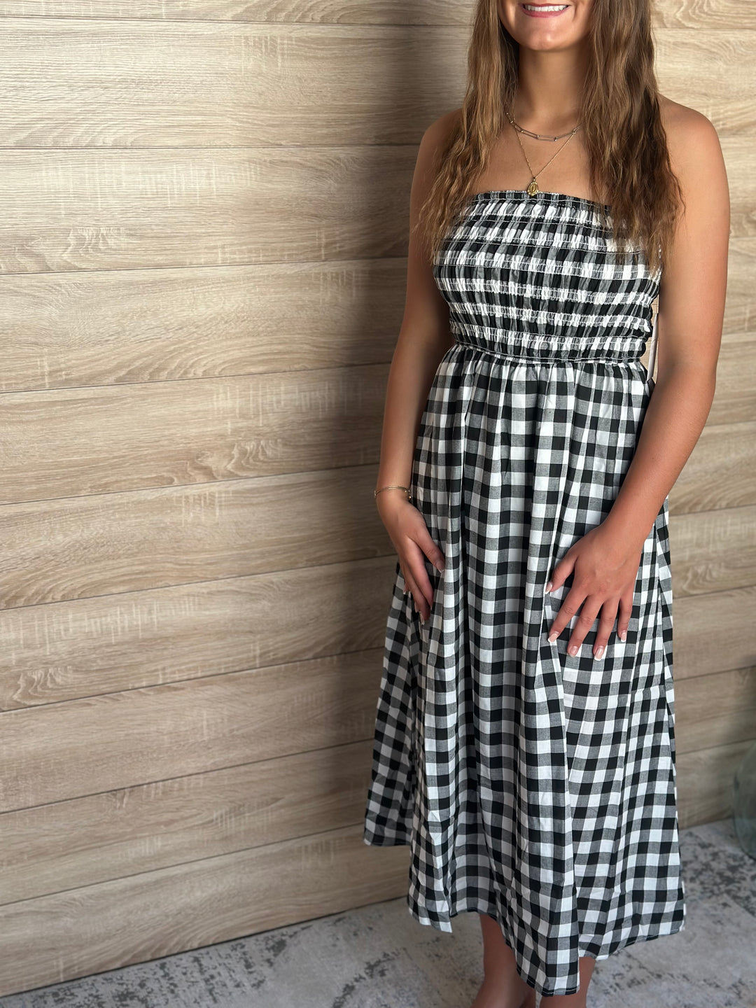 Woman wearing a black and white plaid strapless dress against a wooden paneled wall.