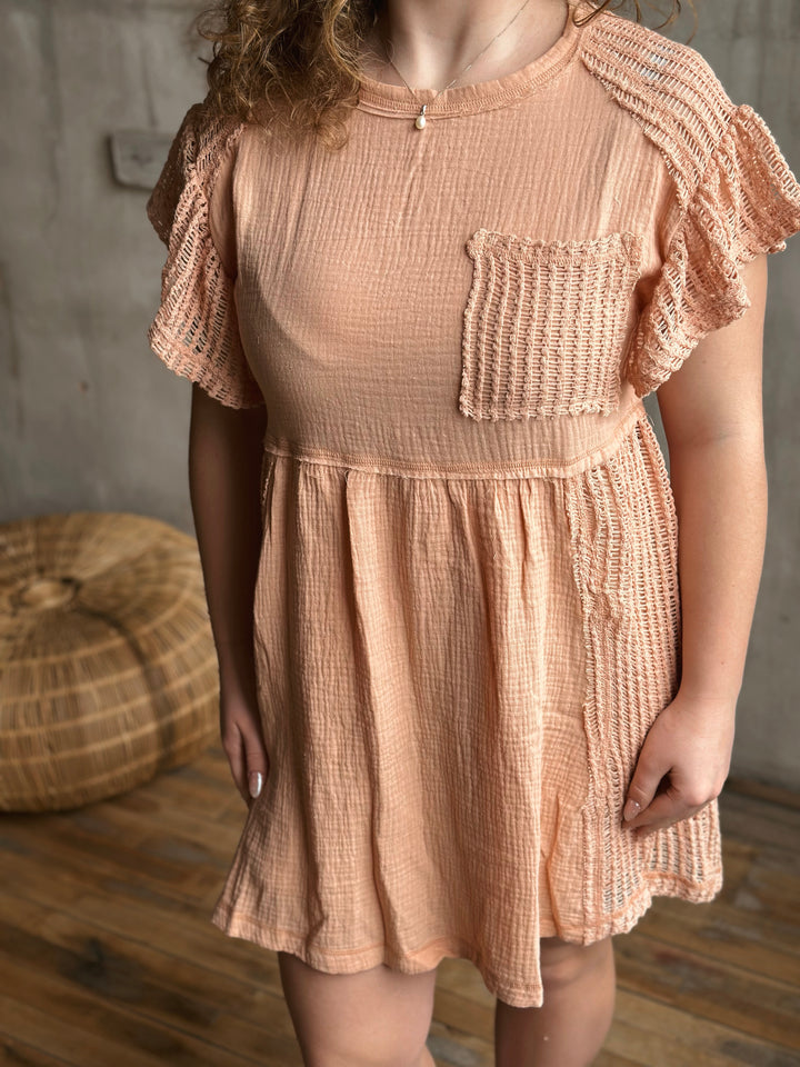 Woman wearing a peach-colored dress with ruffled sleeves in a room with wooden flooring.