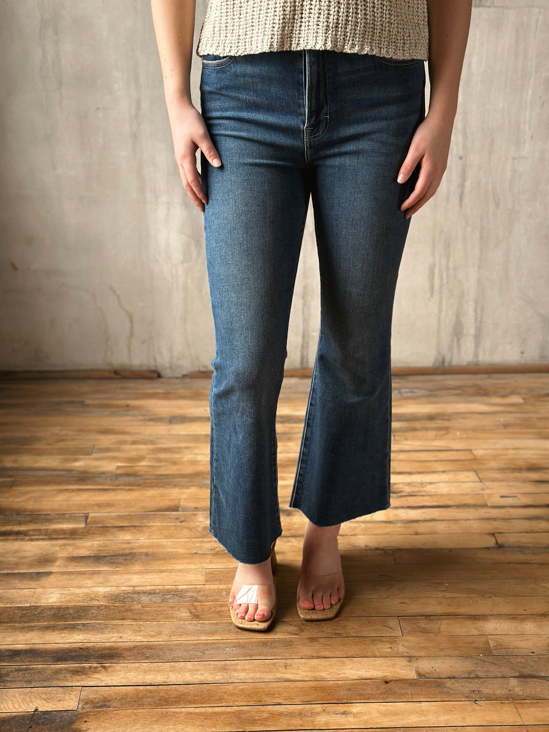 Person wearing blue flared jeans standing on a wooden floor with a neutral wall background