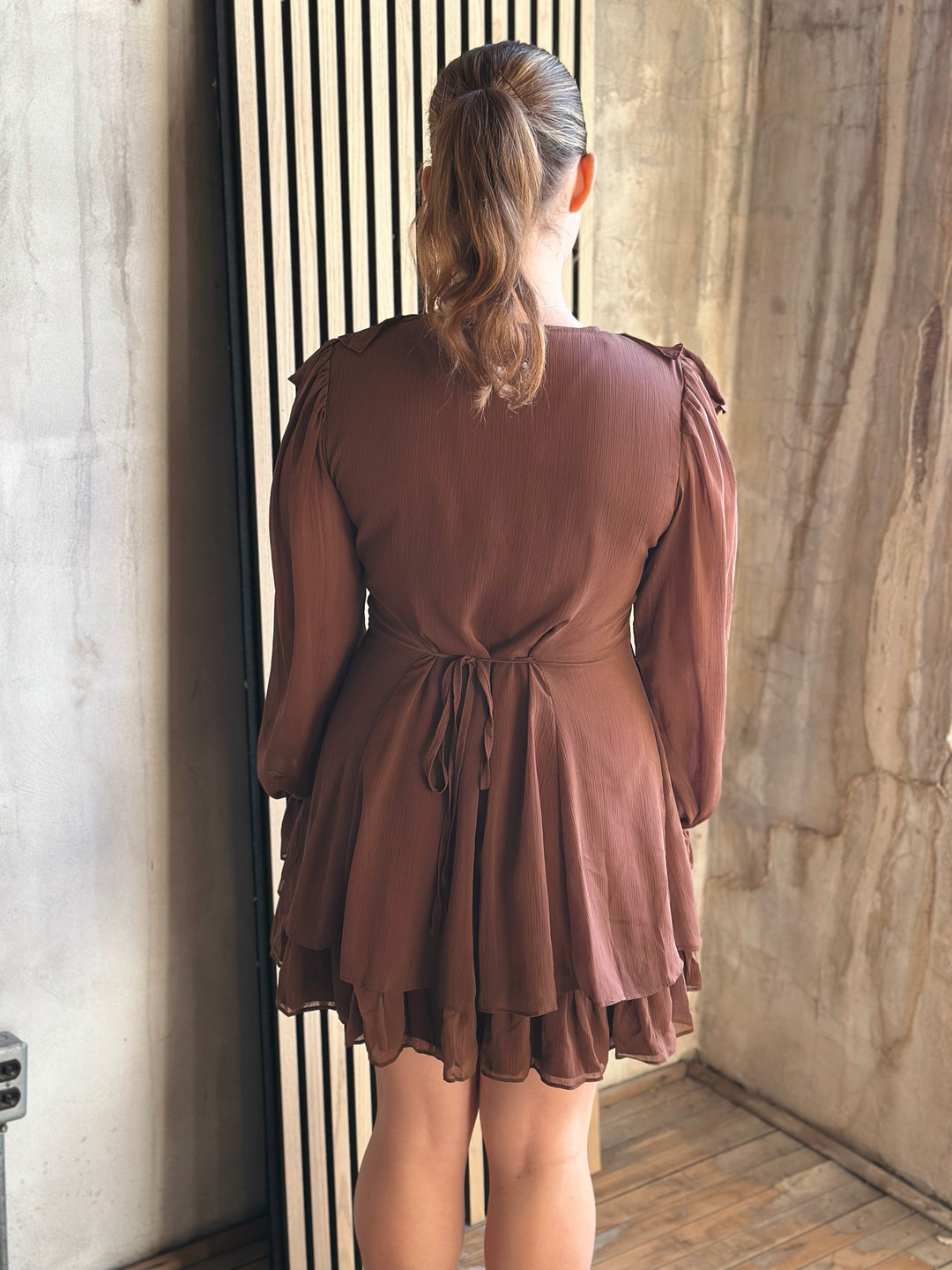Woman wearing a brown dress standing in a room with stone walls.