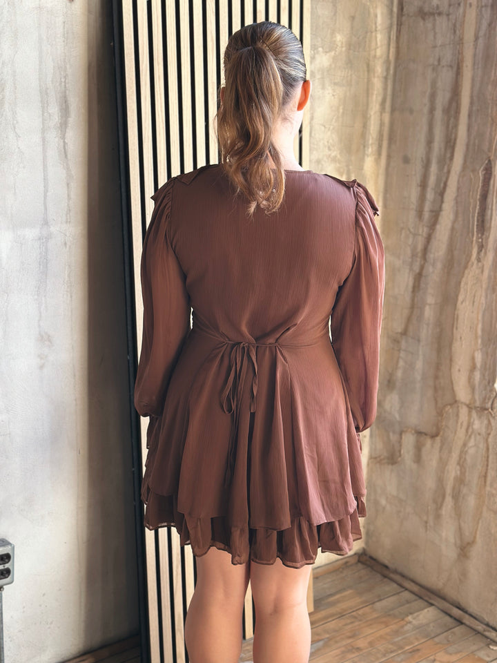 Woman wearing a brown dress standing in a room with stone walls.
