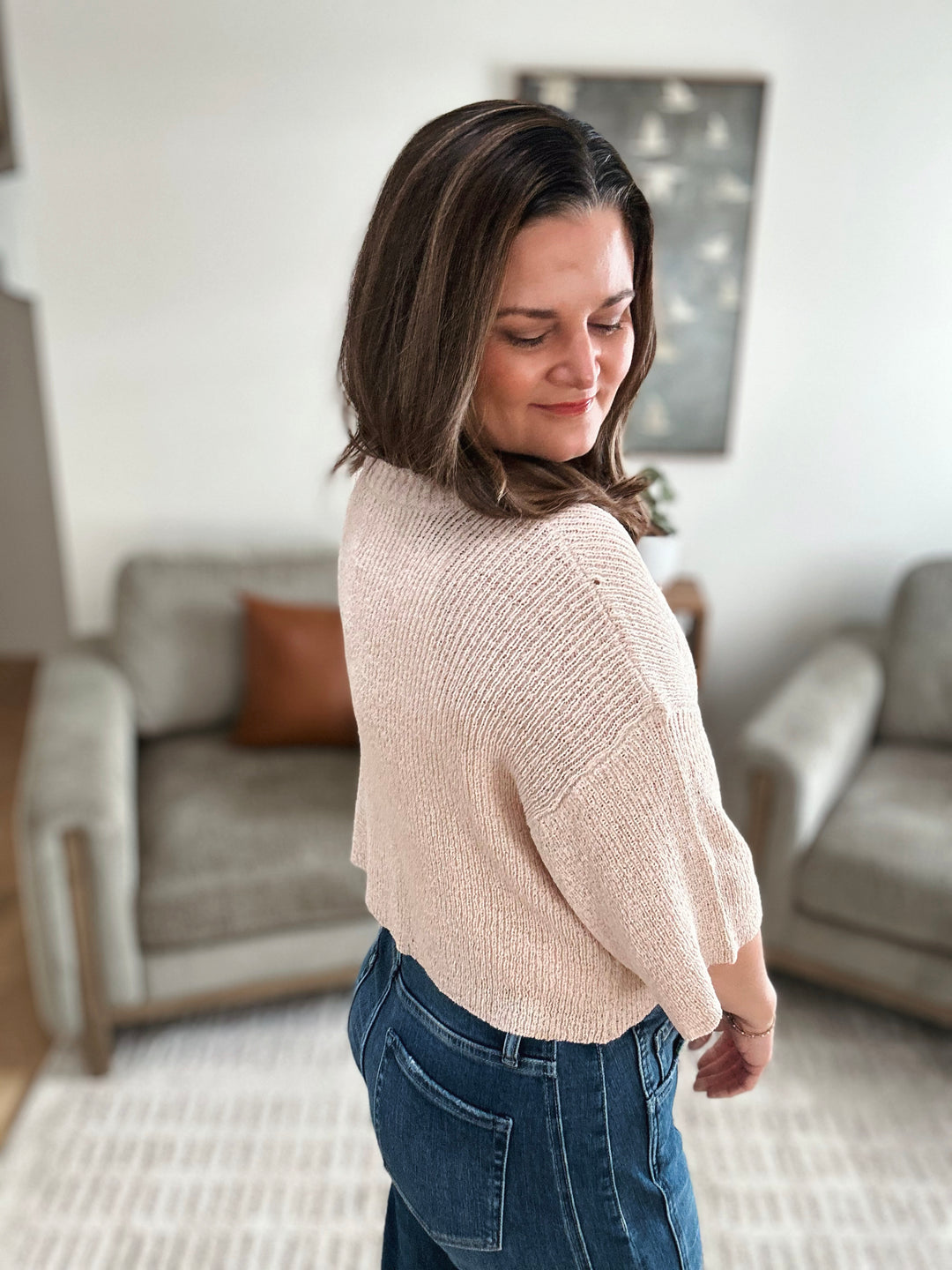 Woman wearing a beige sweater and blue jeans in a living room setting
