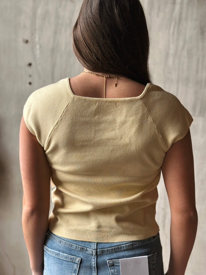 Person wearing a beige top and blue jeans against a neutral background
