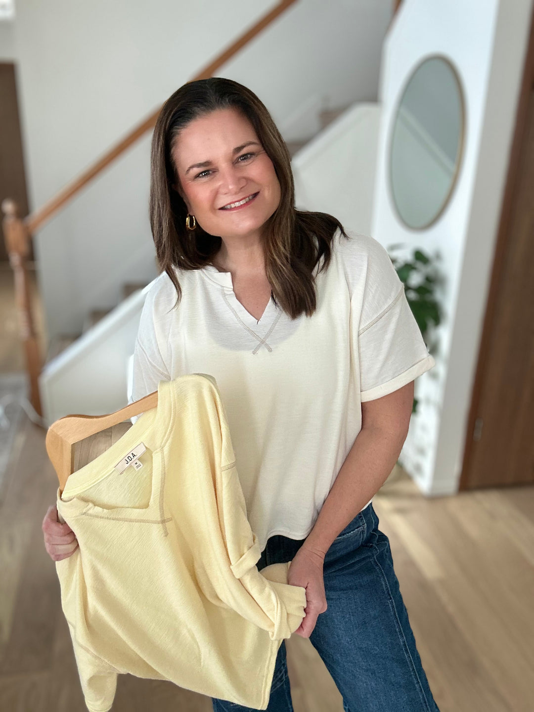 Woman holding a yellow v-neck t-shirt and wearing a white v-neck t-shirt in a home setting