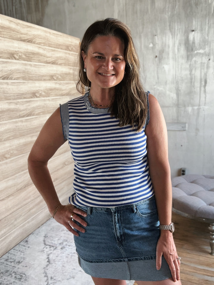 Woman wearing a blue and white striped shirt and denim skirt standing indoors.