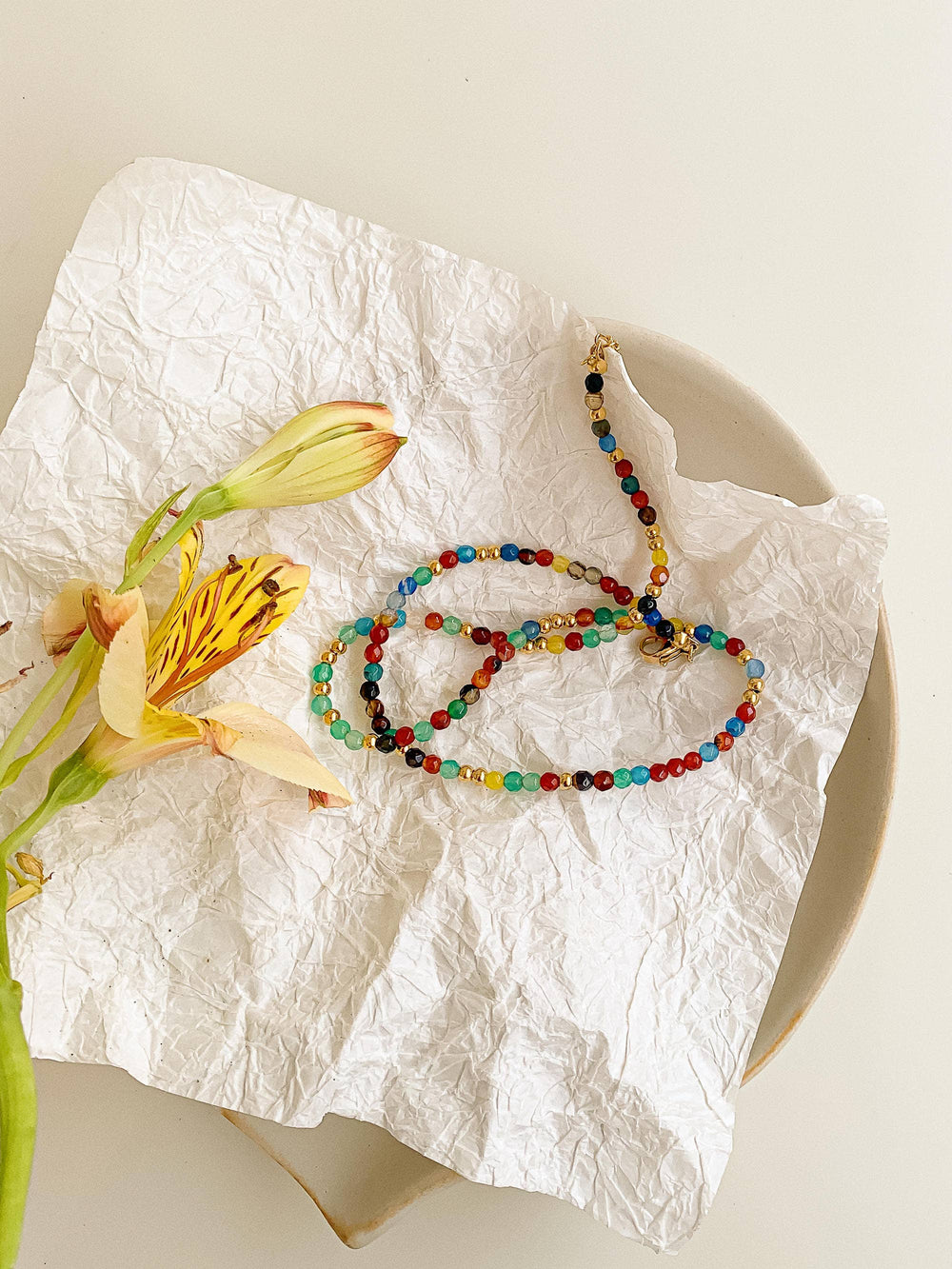 Colorful beaded necklace on crumpled white paper with a flower beside it