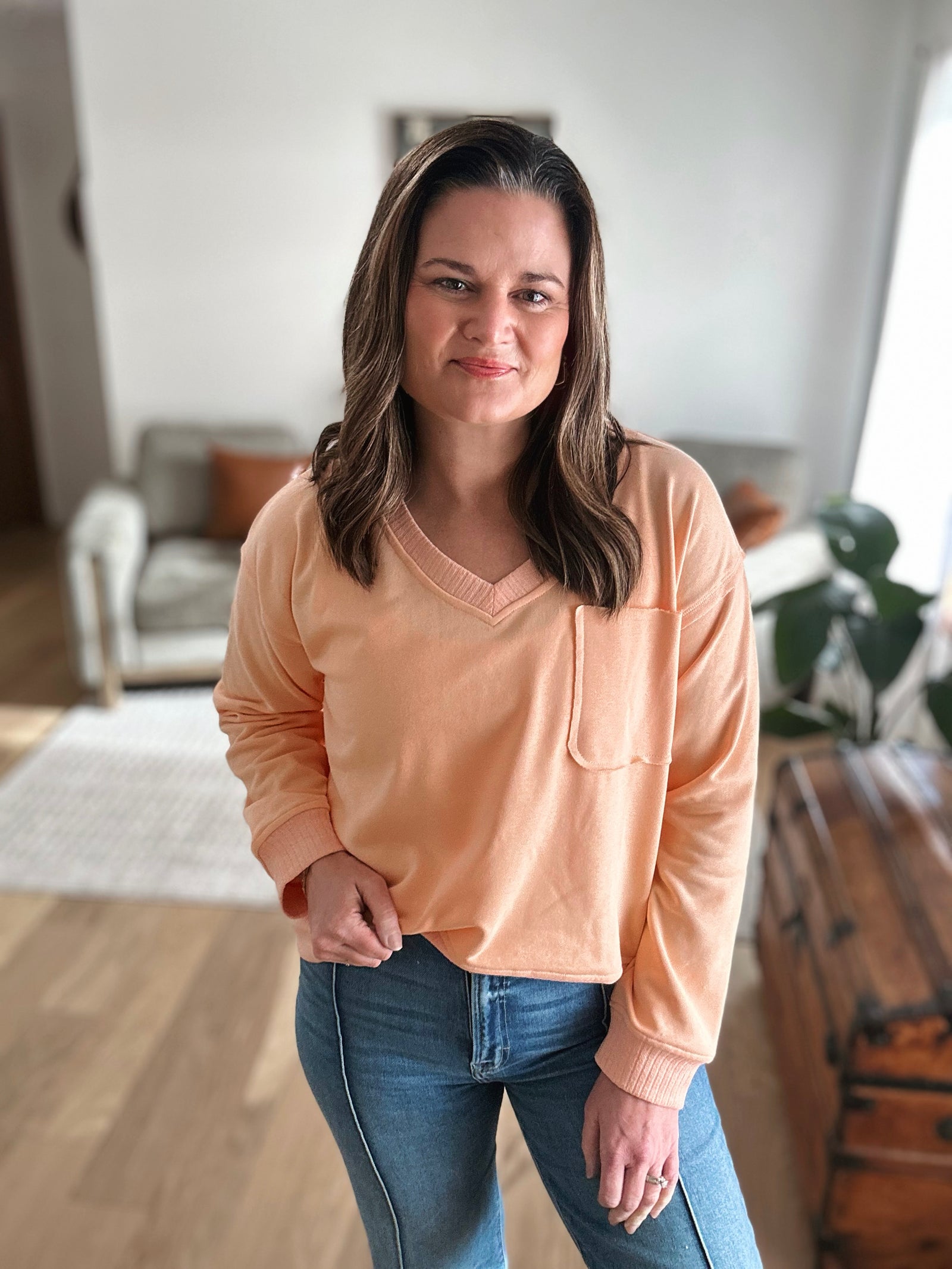 Woman wearing a peach sweater and blue jeans indoors