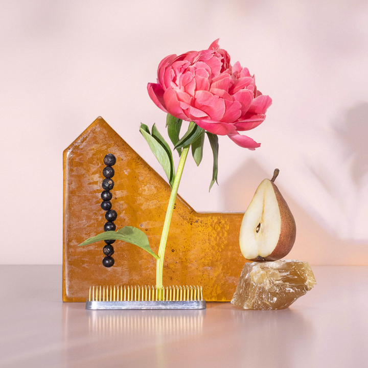 Decorative object with a pink flower, pear, and comb on a reflective surface.
