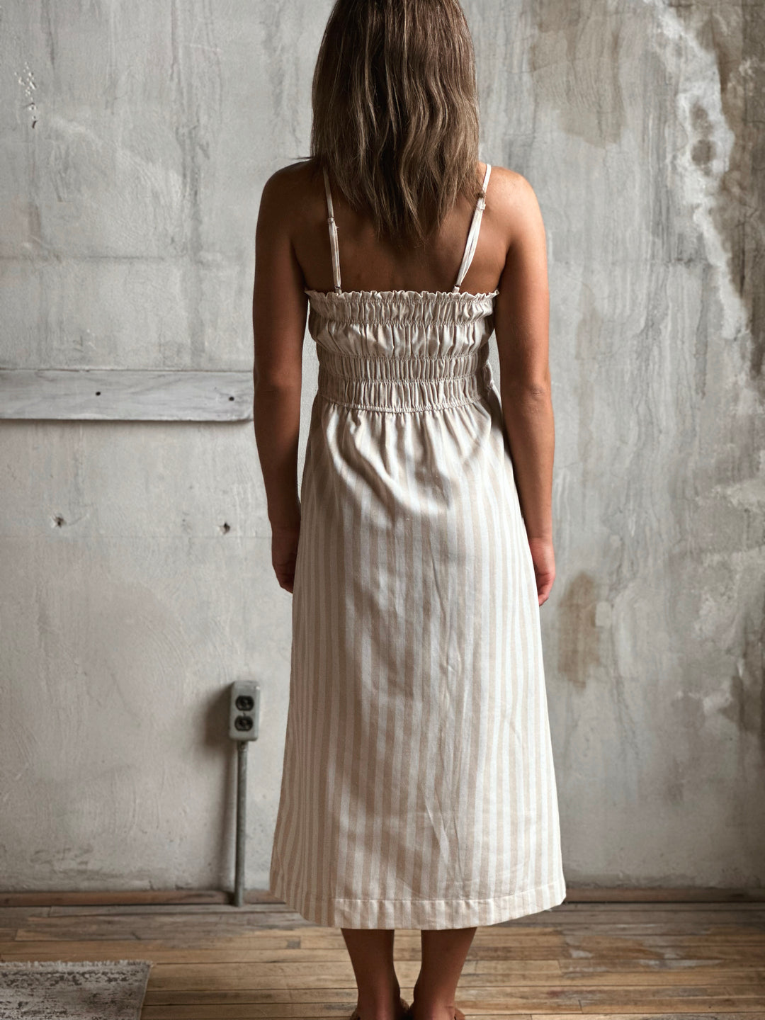 Woman wearing a white and cream striped dress standing against a textured wall.