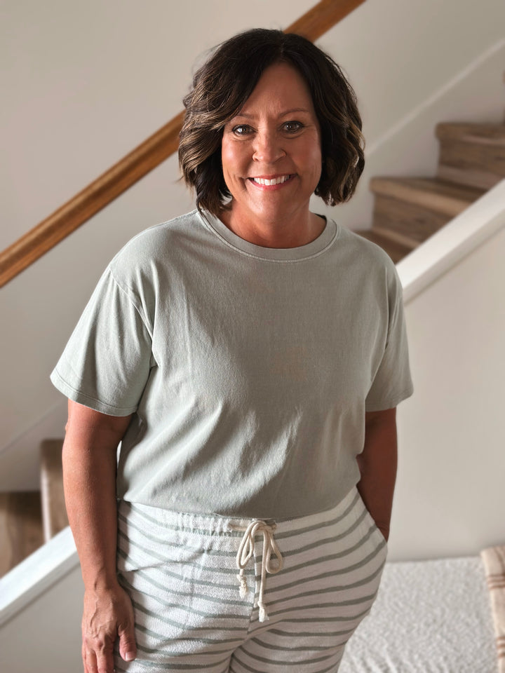 Woman wearing a light green t-shirt and striped pants standing indoors.