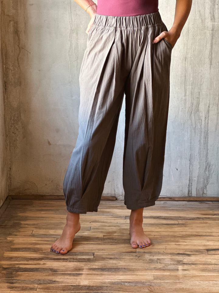 Person wearing brown wide-leg pants and a pink top against a textured wall.