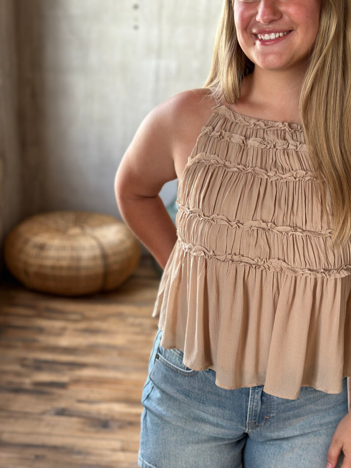 Woman wearing a beige sleeveless top and blue denim shorts indoors.