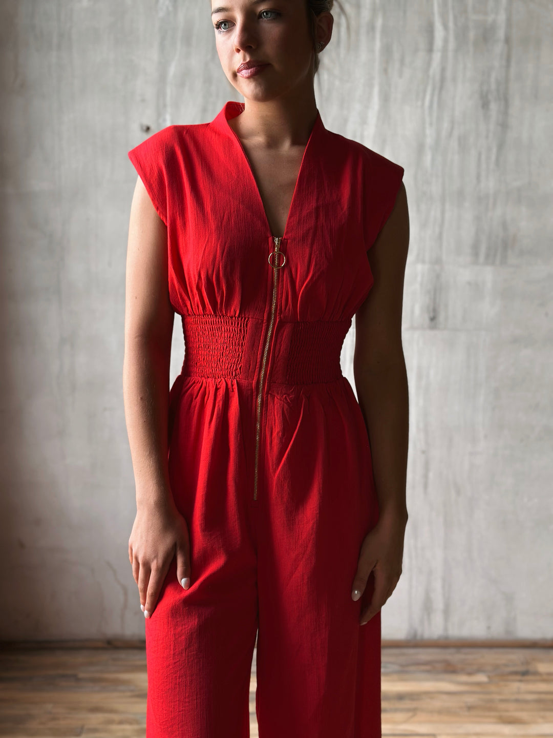 Close up Front view of red sleeveless jumpsuit features a flattering v-neckline, a front zipper closure, and a smocked waist