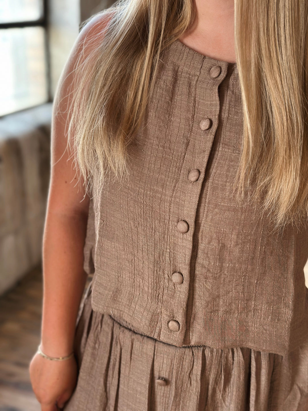Brown button-up sleeveless top worn by a person with blurred background.
