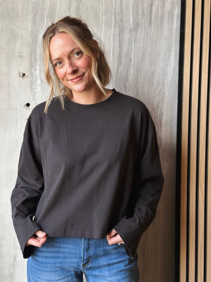 Person wearing a black sweatshirt and blue jeans standing against a textured wall.