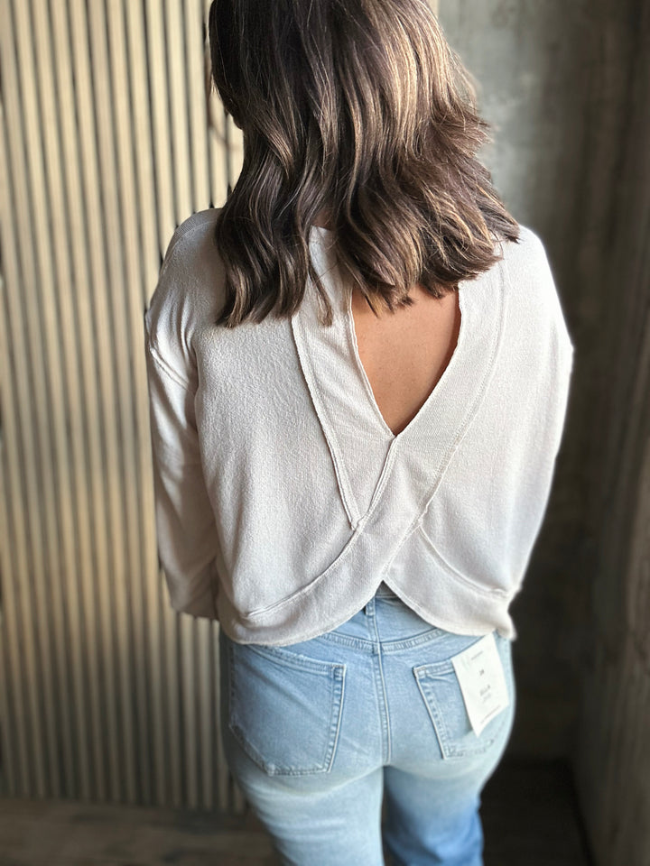 Person wearing a light-colored sweater with a backless design and light blue jeans.
