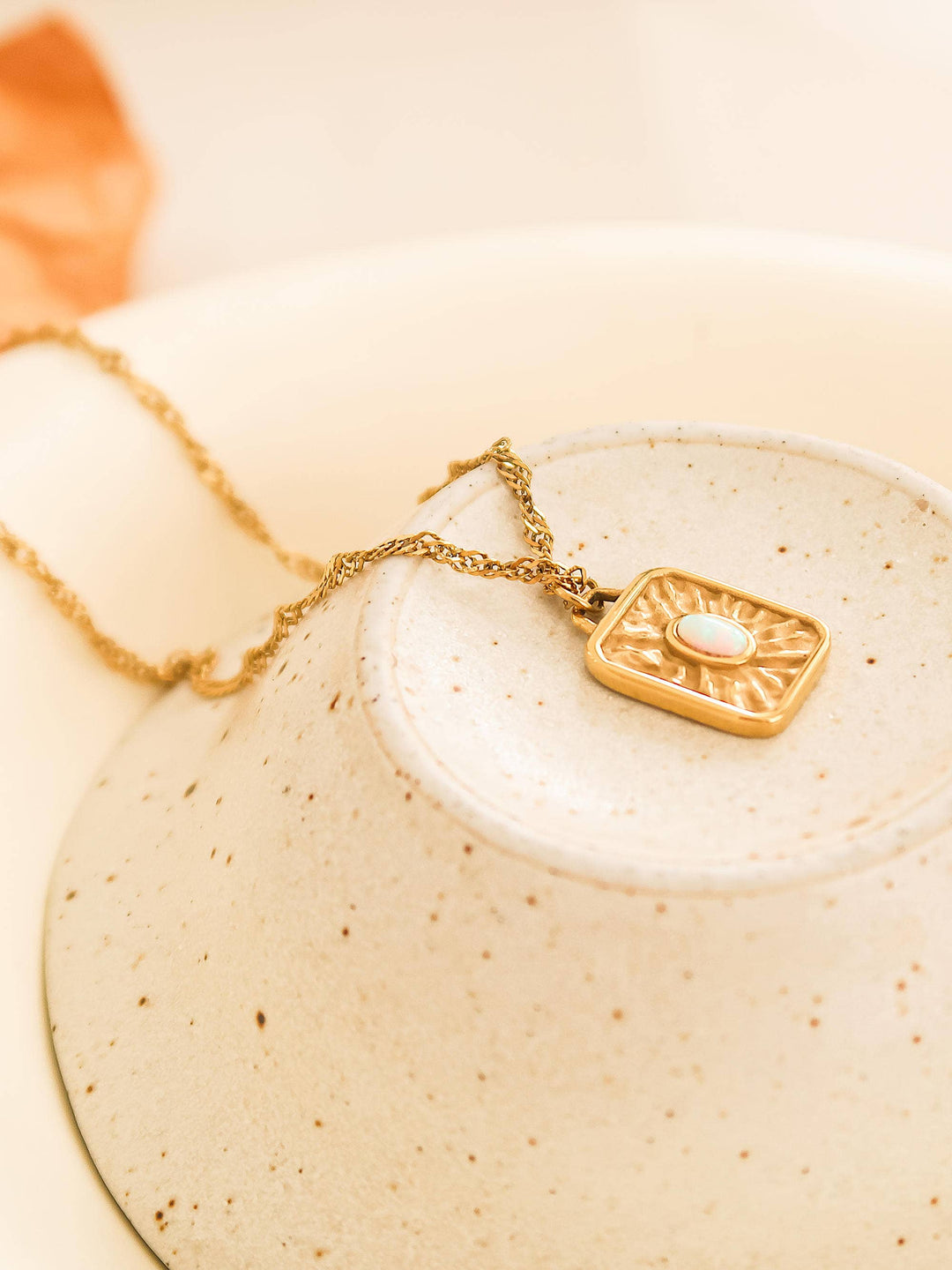 Gold necklace with a square pendant on a beige ceramic plate