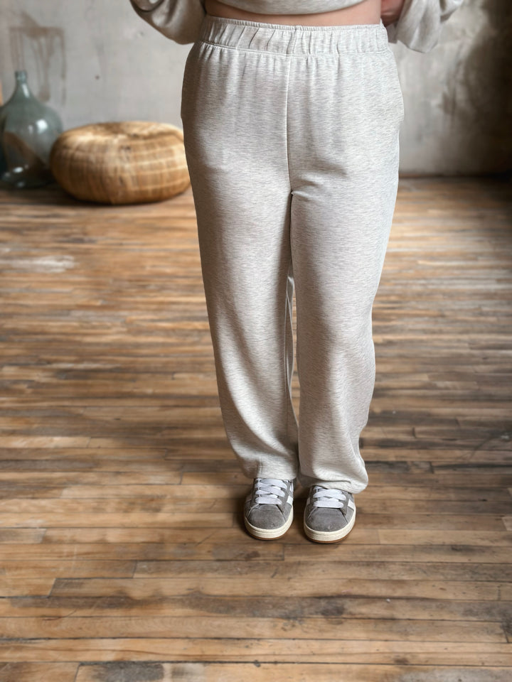 Person wearing light grey sweatpants standing on a wooden floor.
