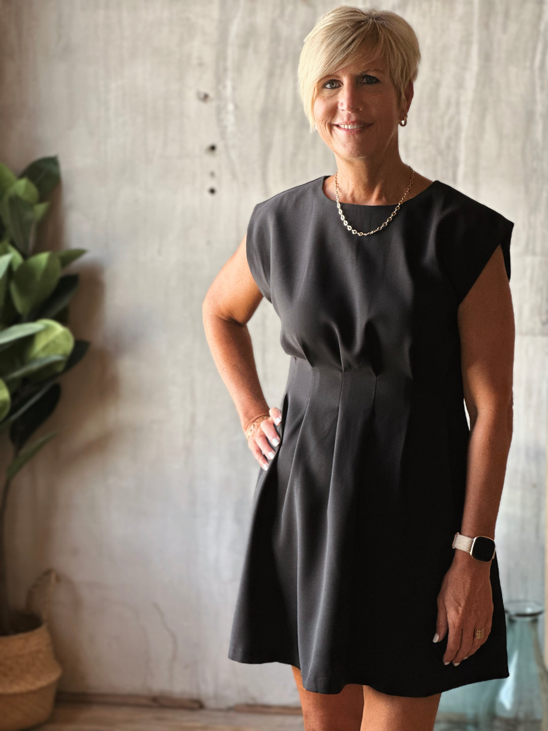 Woman wearing a black dress standing indoors with a neutral background