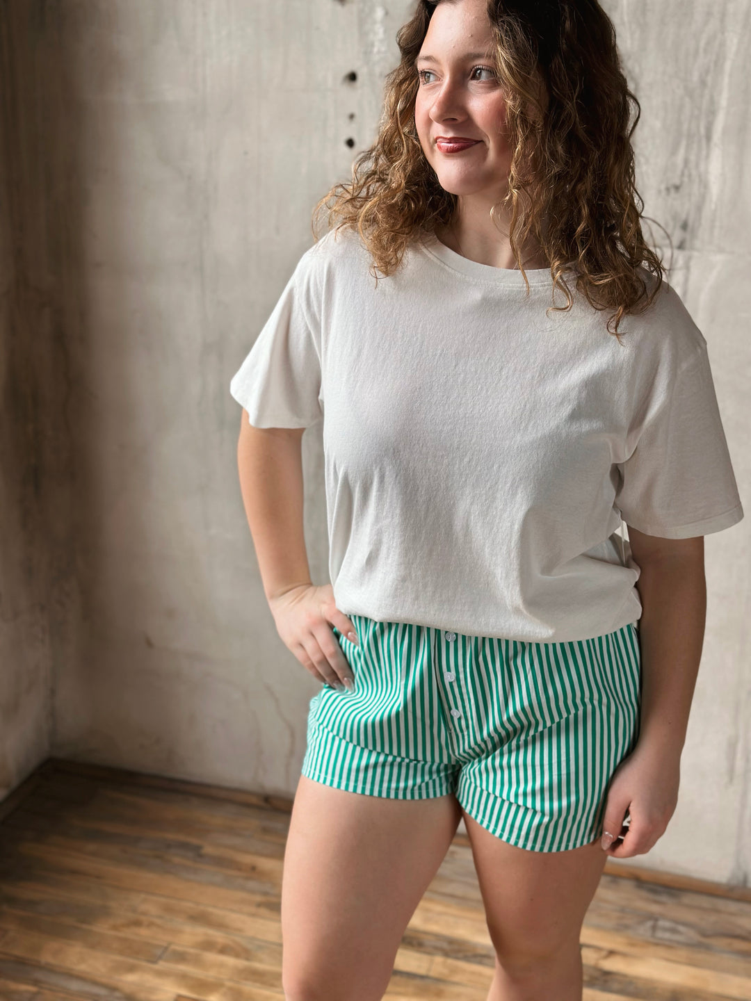 Woman wearing a white t-shirt and green striped shorts standing against a neutral wall.