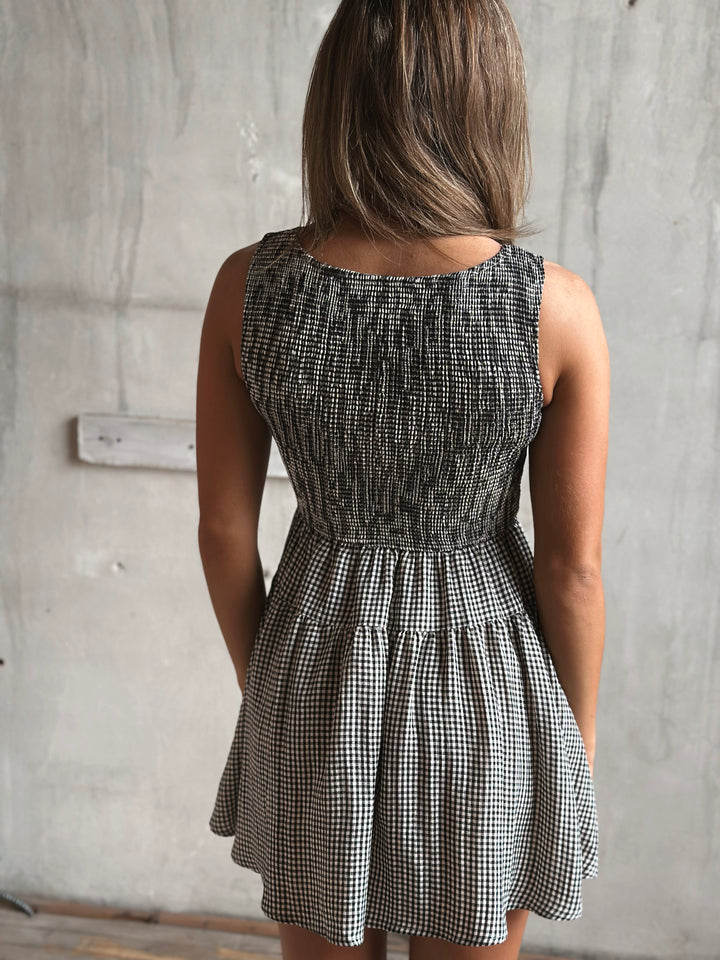 Person wearing a black and white gingham dress against a gray wall.