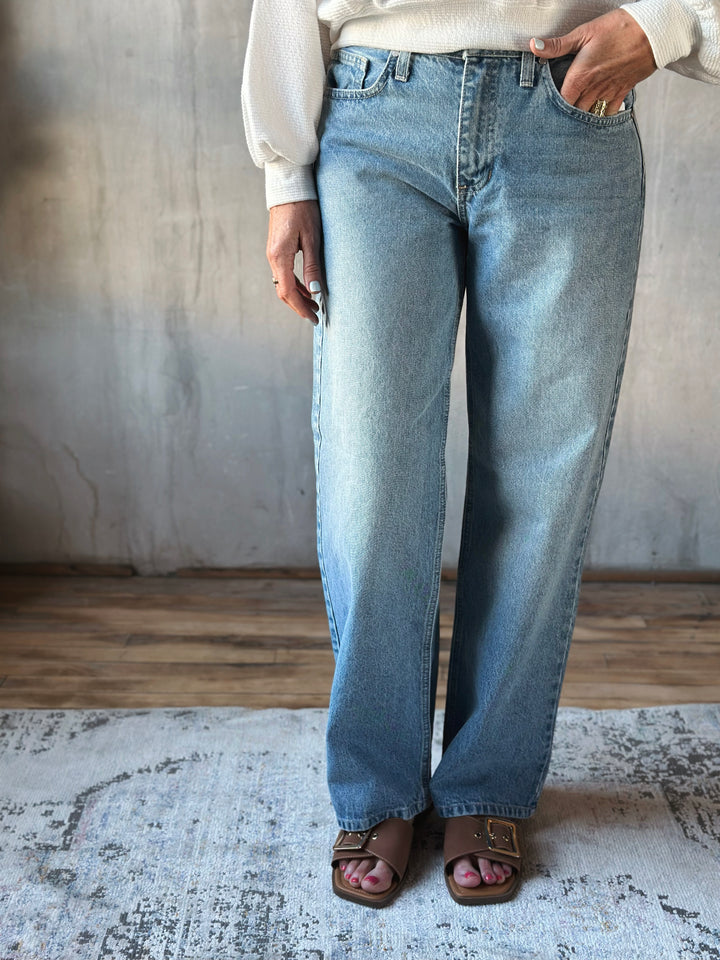 Person wearing light blue jeans standing on a textured rug with a neutral background