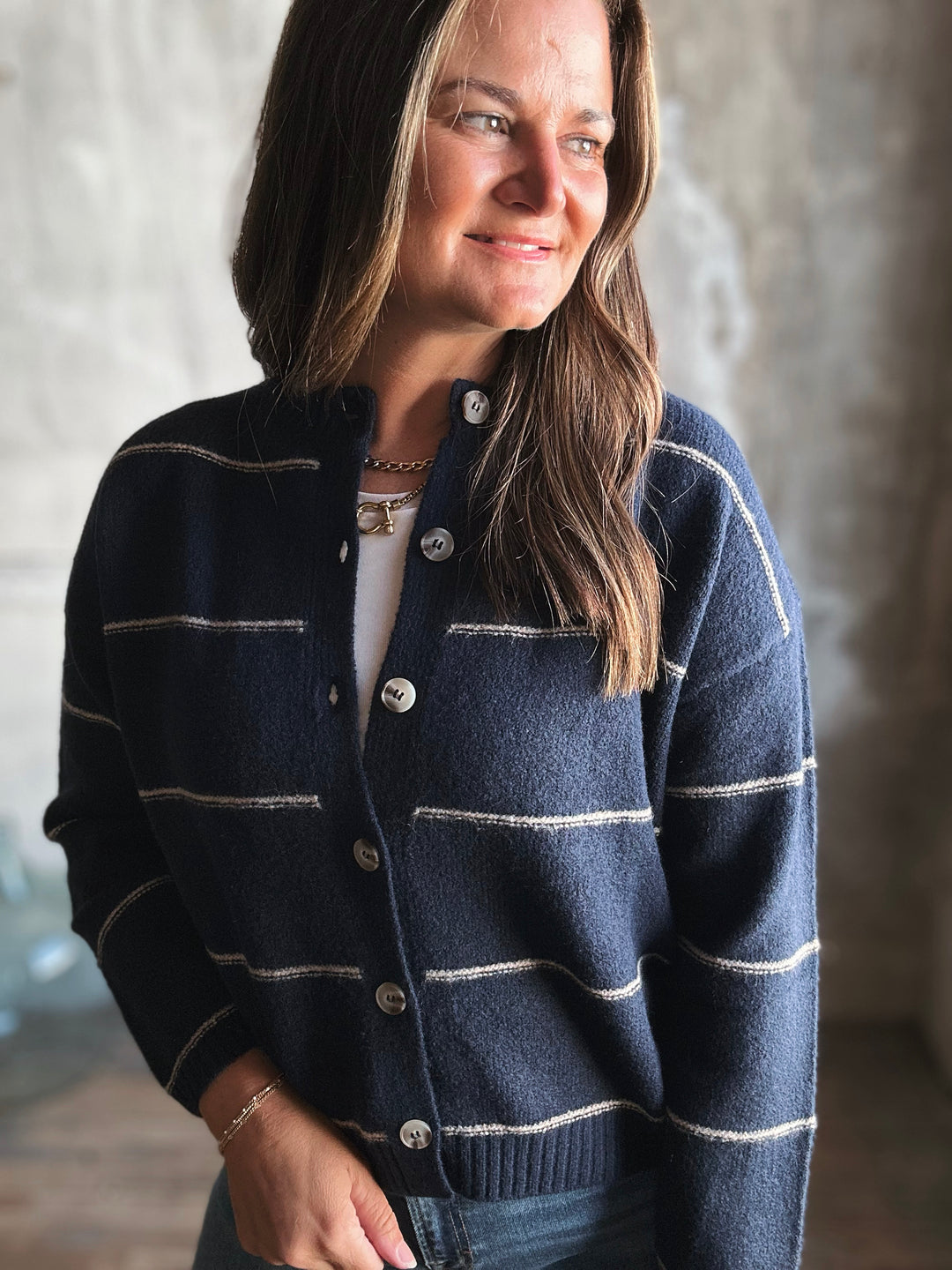 Woman wearing a navy blue cardigan with white stripes against a neutral background