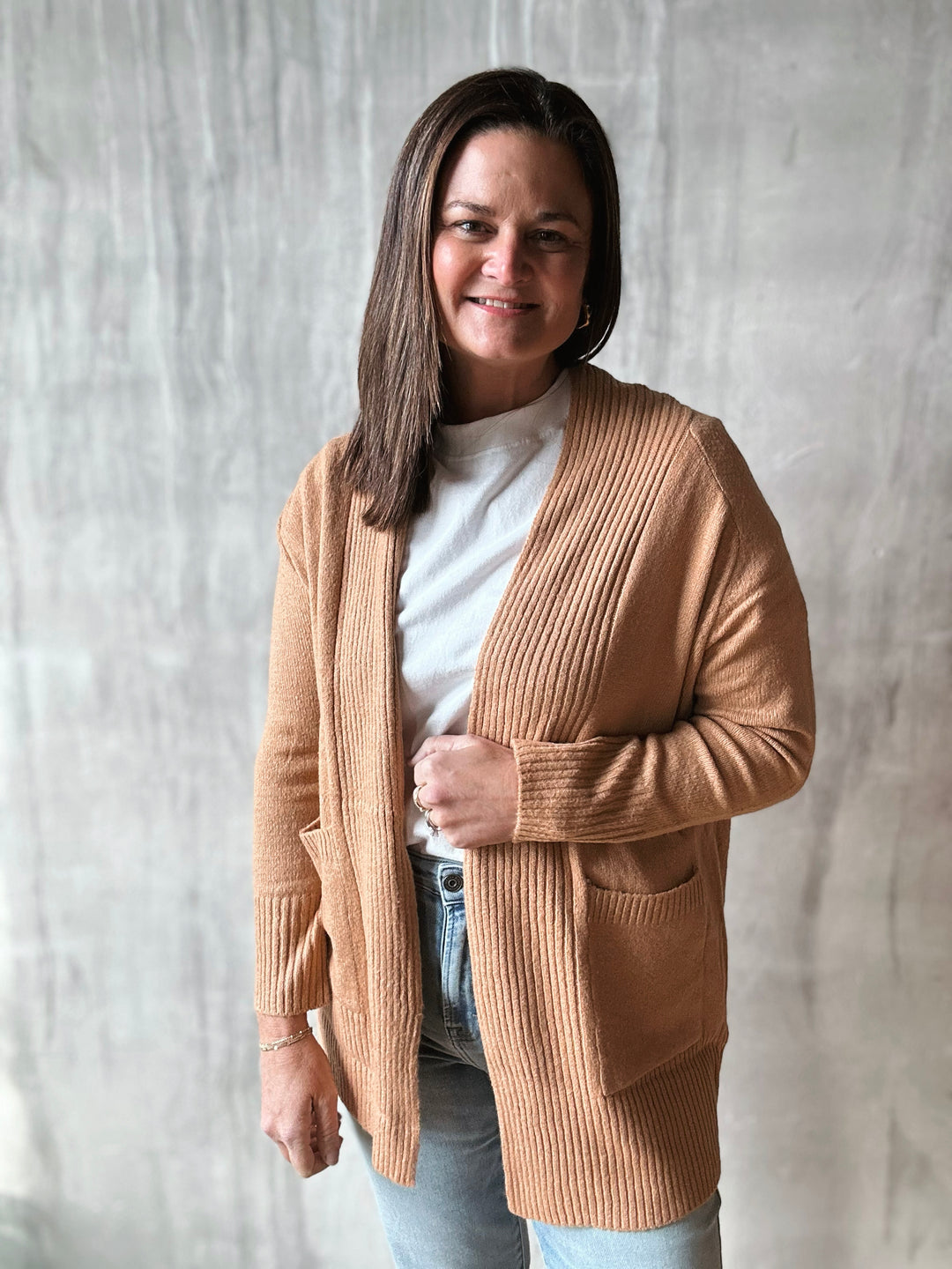 Woman wearing a beige cardigan over a white shirt with a neutral background