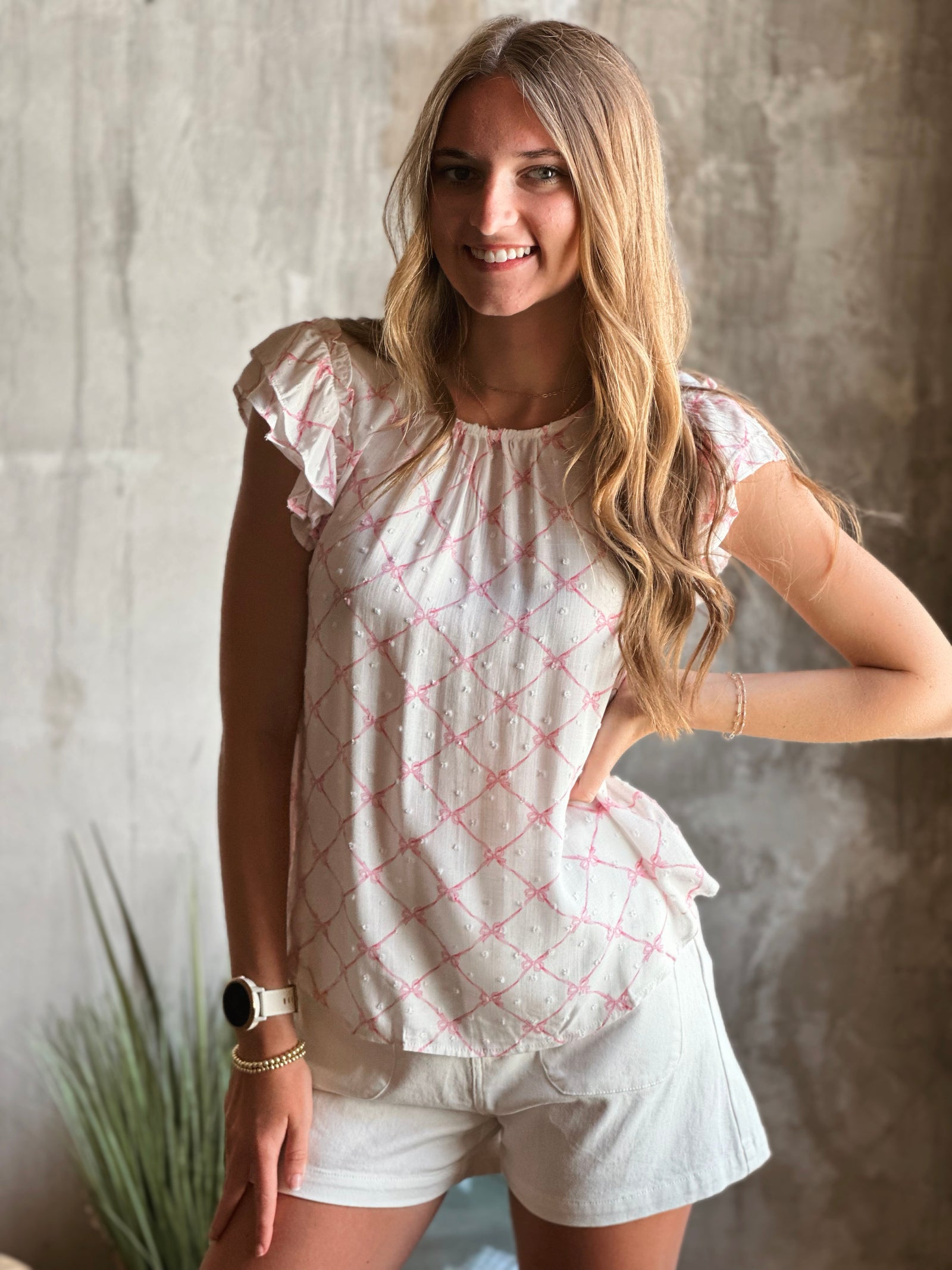 Front view of model wearing all over pink bow pattern ruffle sleeve top with a white background