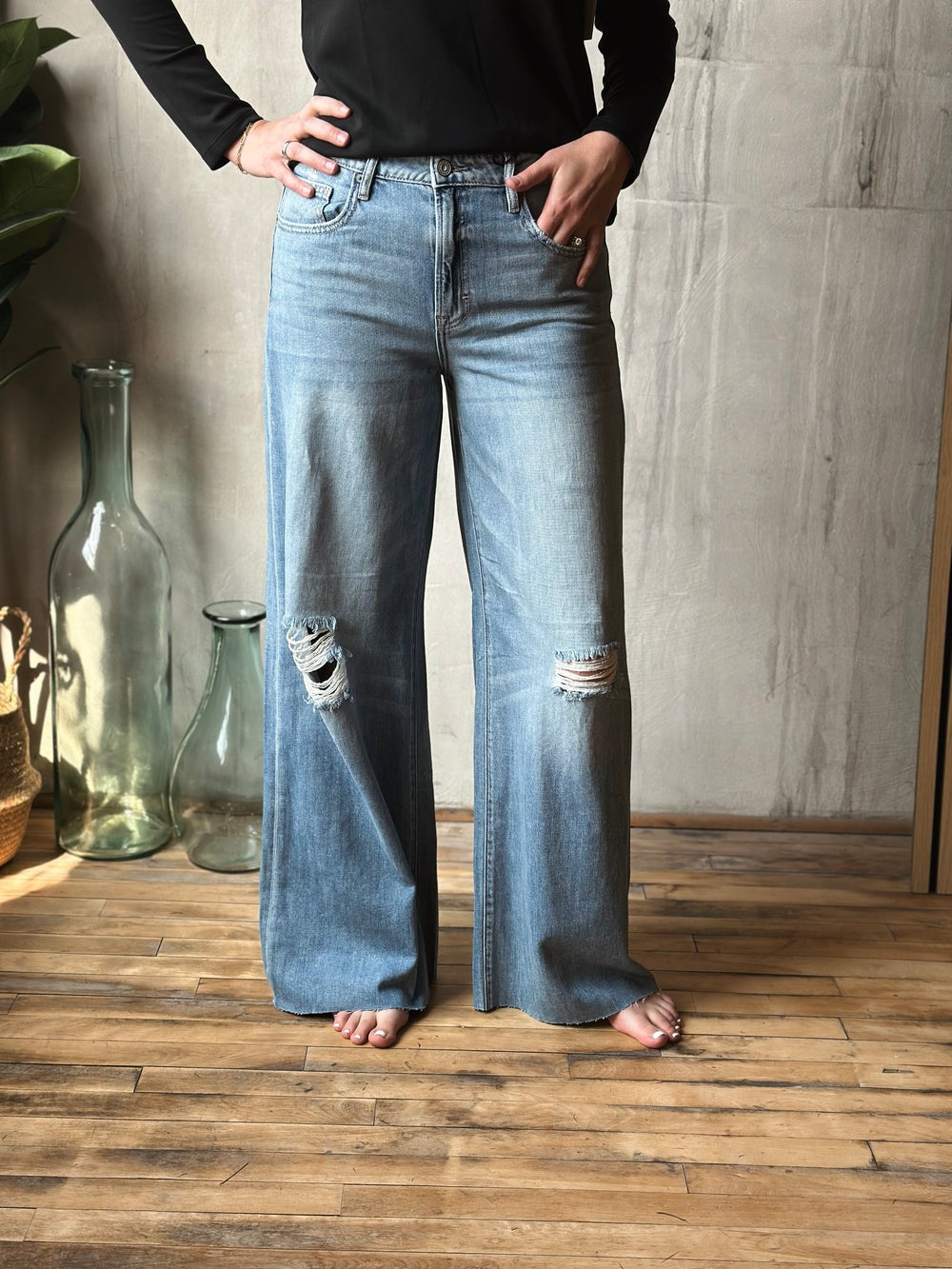 Person wearing light blue distressed wide-leg jeans standing on a wooden floor.