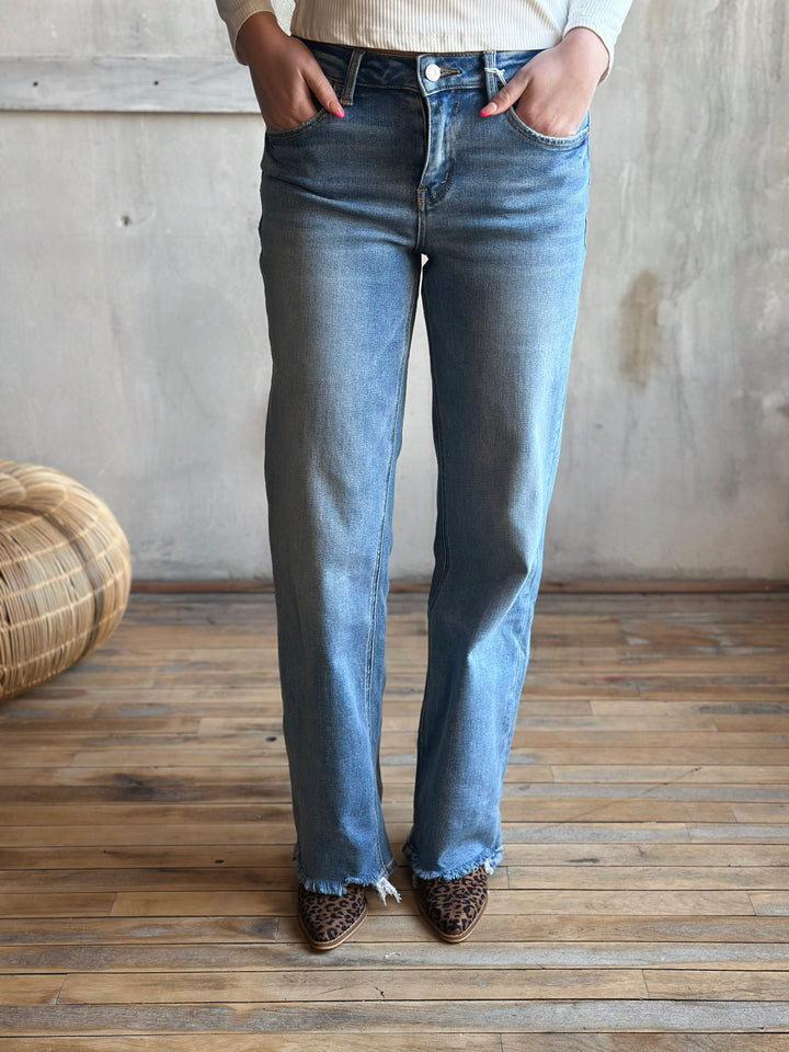 Person wearing light blue jeans standing in a room with wooden flooring and a textured wall.
