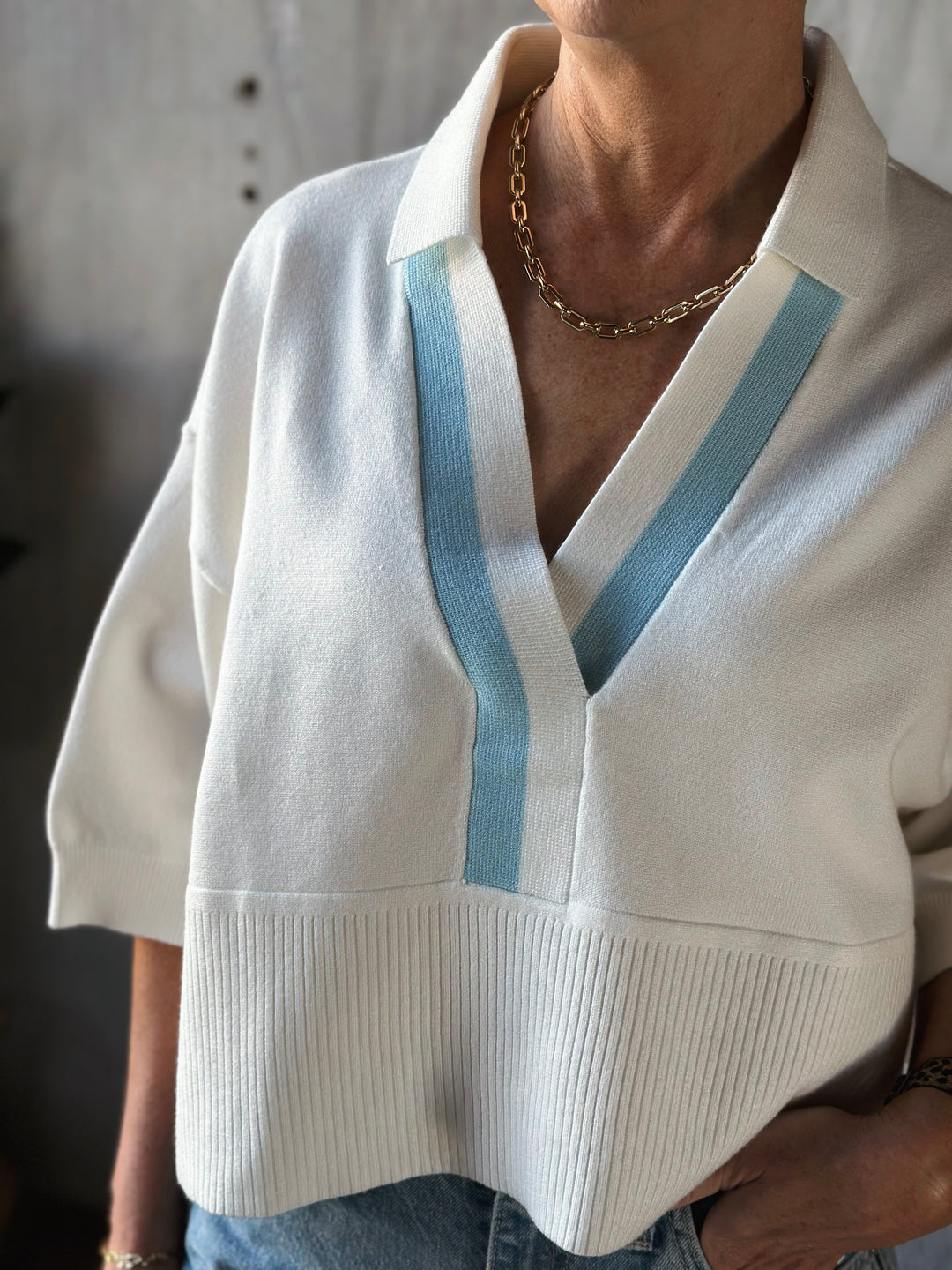White sweater with blue trim worn by a person, with a neutral background